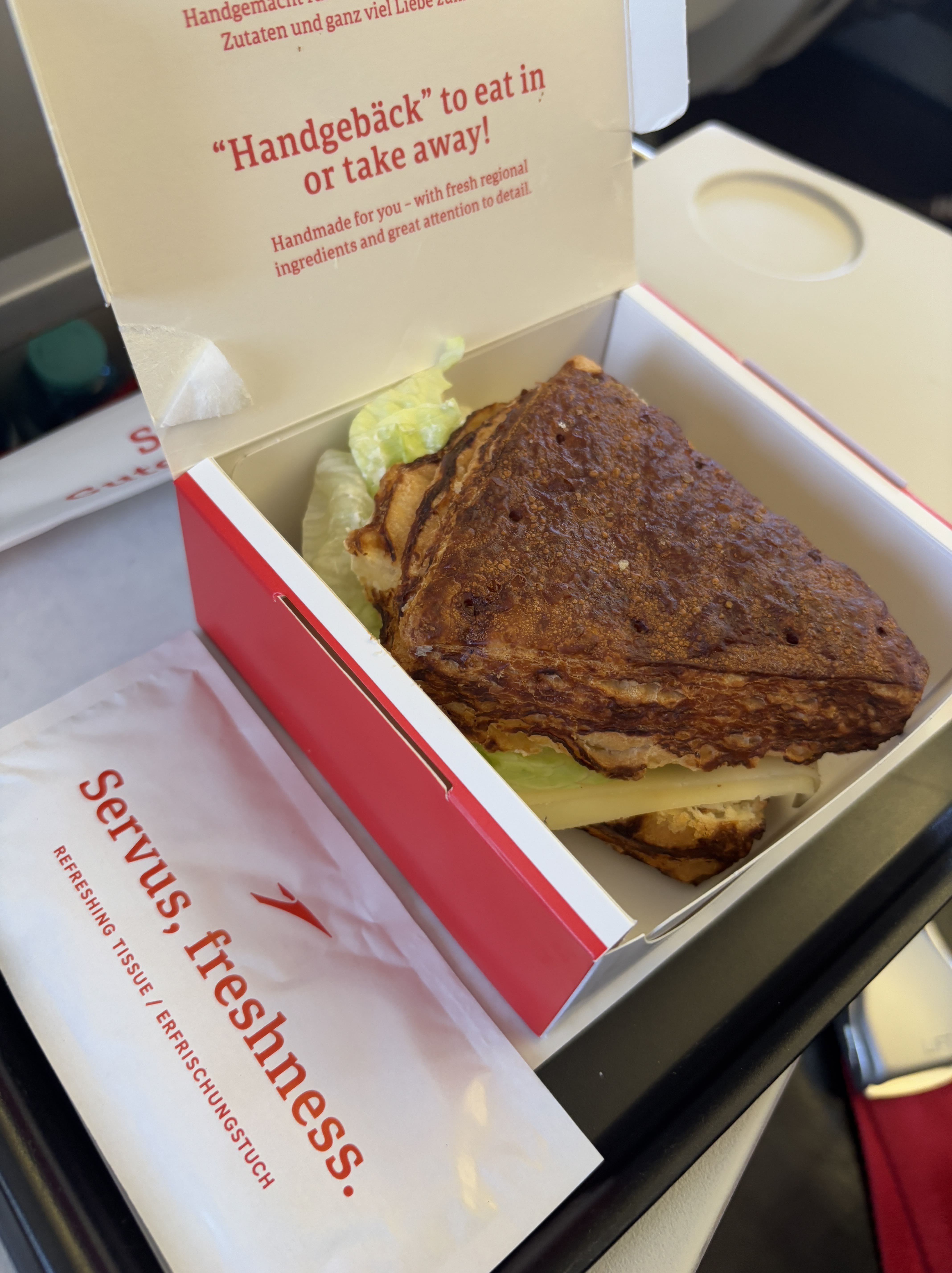 Triangular sandwich in a red paper box, moist towelette served alongside.