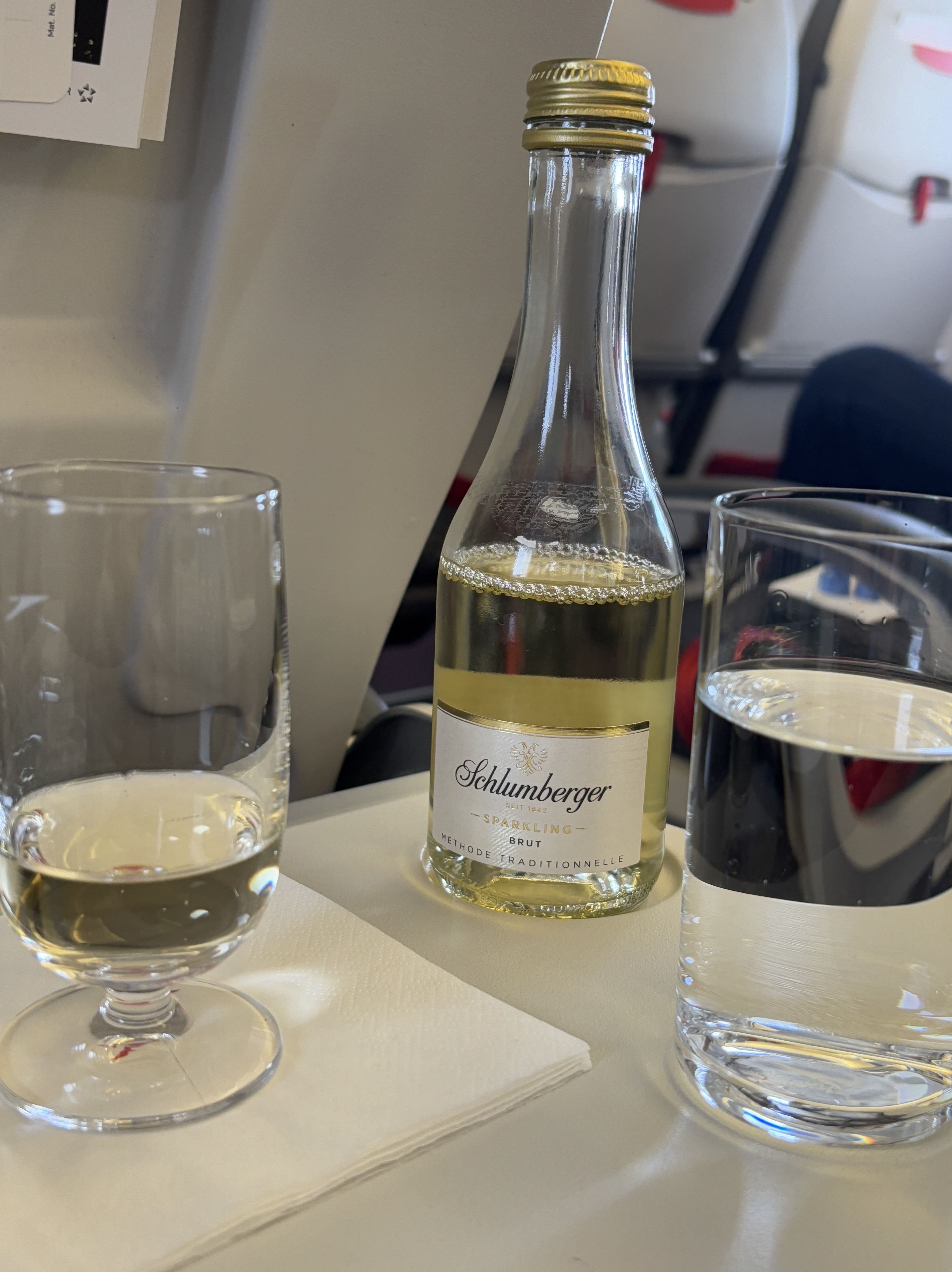 Small bottle of sparkling wine with glasses on either side, one containing some of the wine, the other still water.