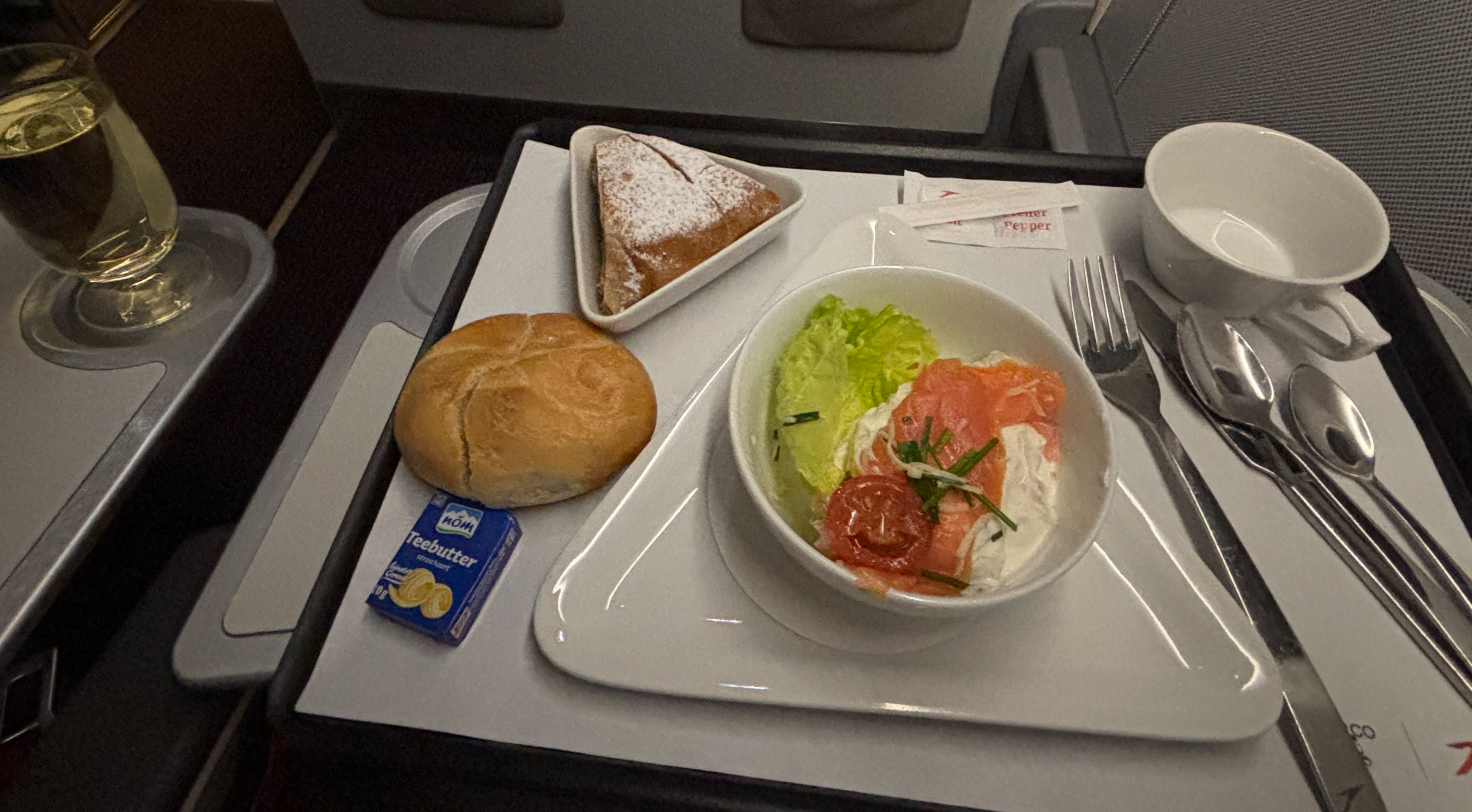 From left to right: glass of white wine, white bread roll with butter, apple strudel, main course of salmon and cream cheese, empty tea cup.