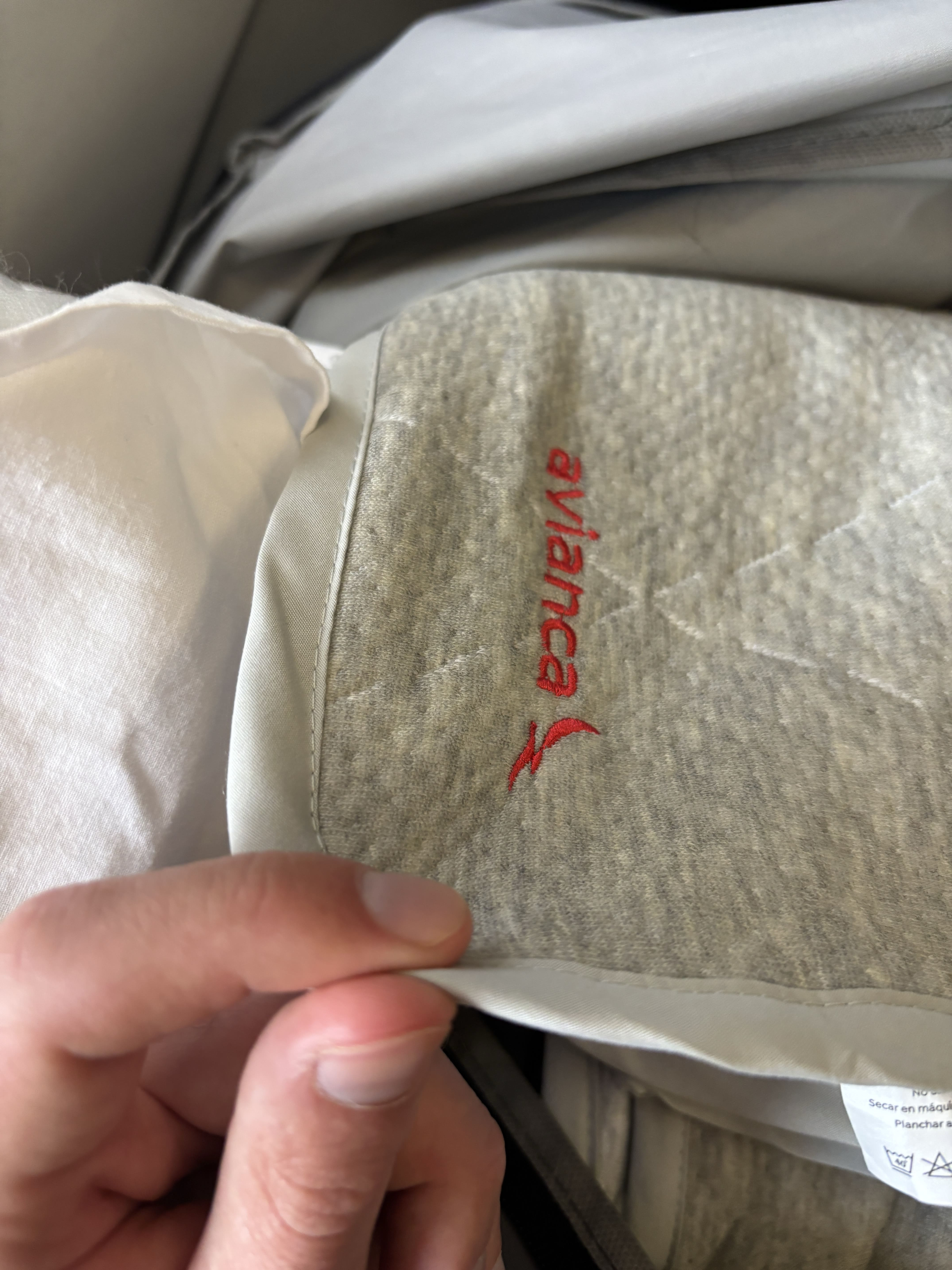 Thin grey blanket with red Avianca logo, being compressed between a forefinger and thumb.