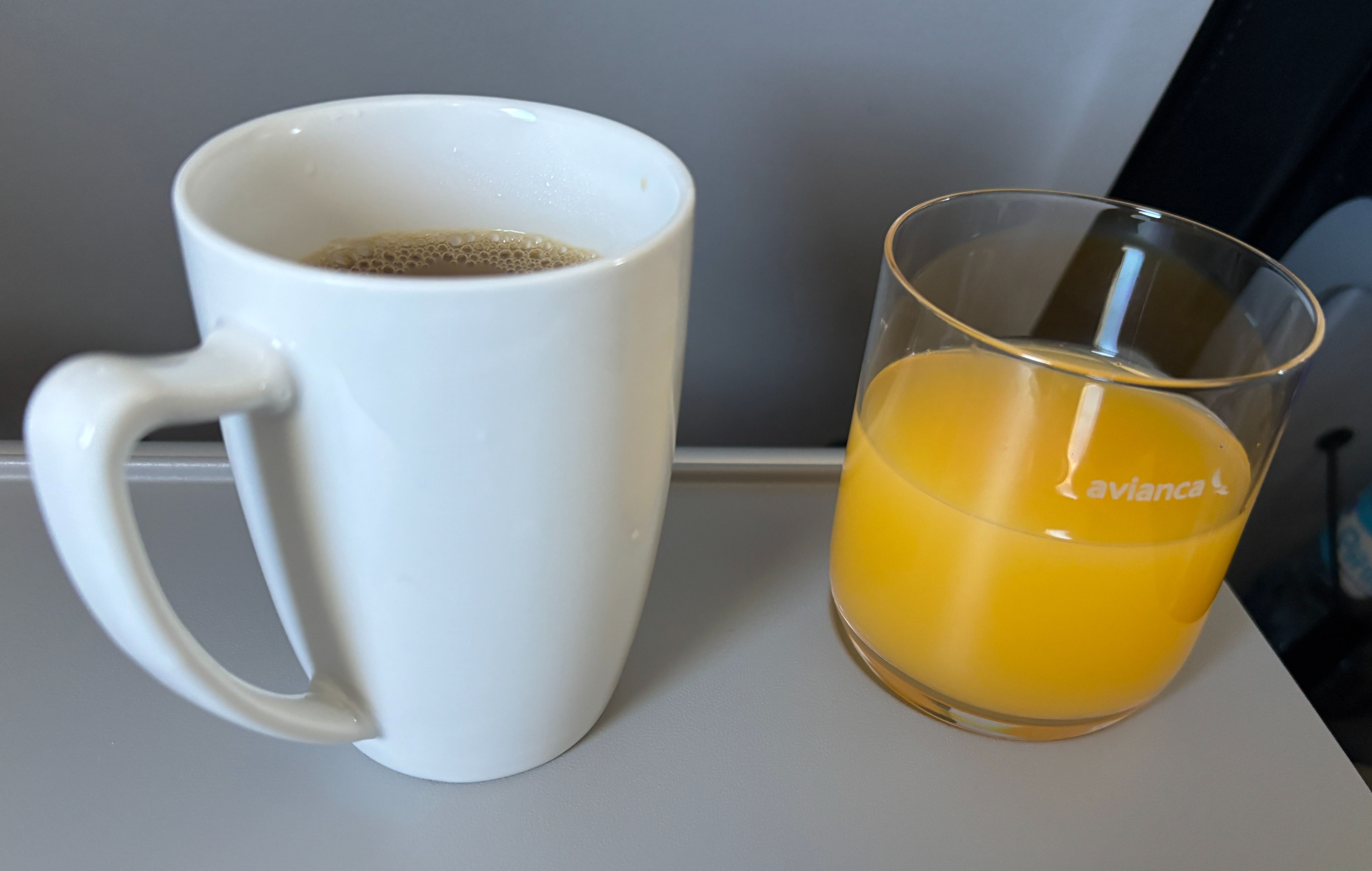 Coffee in a ceramic mug and orange juice in an Avianca-branded glass resting on a tray table.