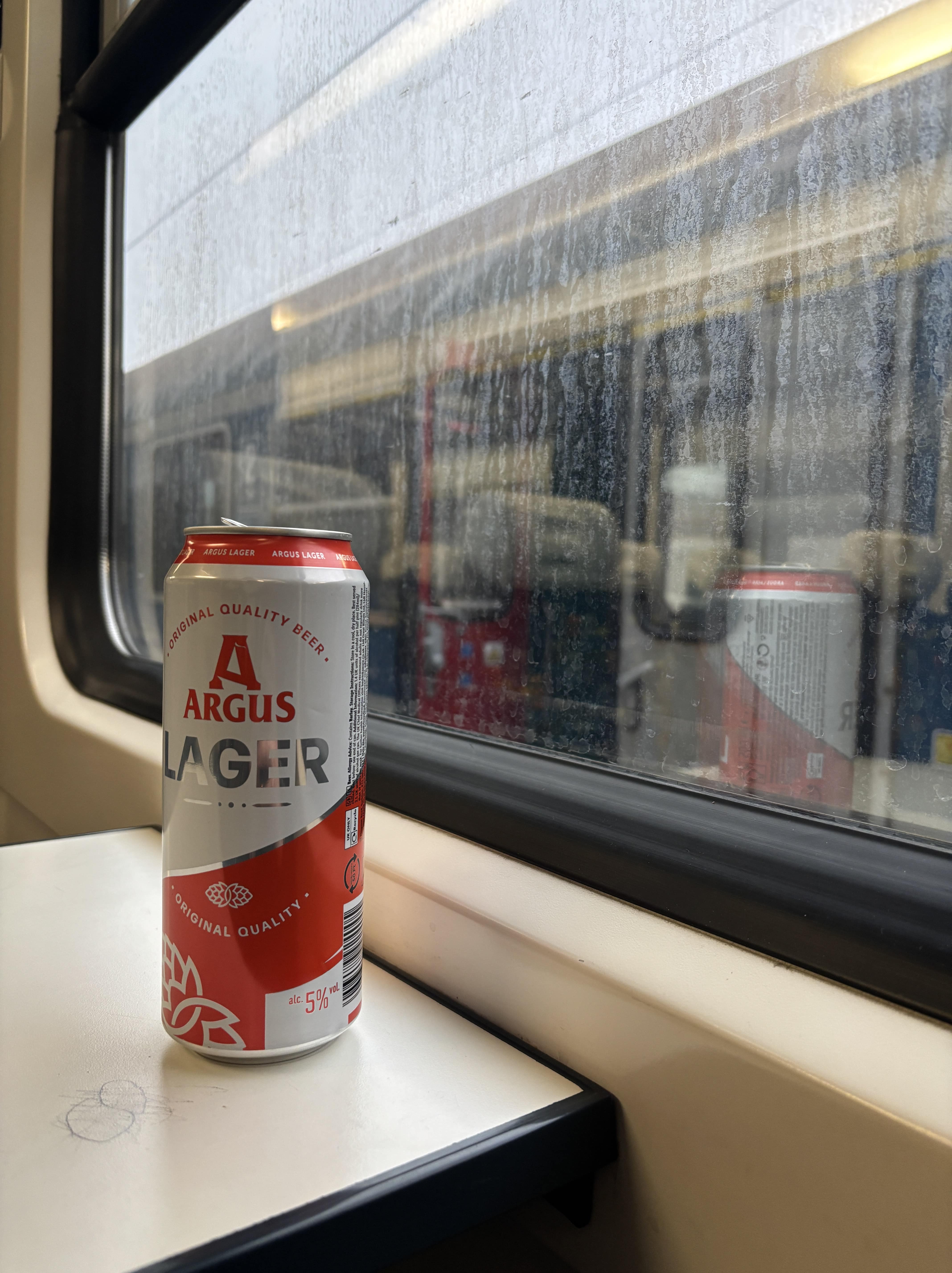 Can of lager next to dirty train window.