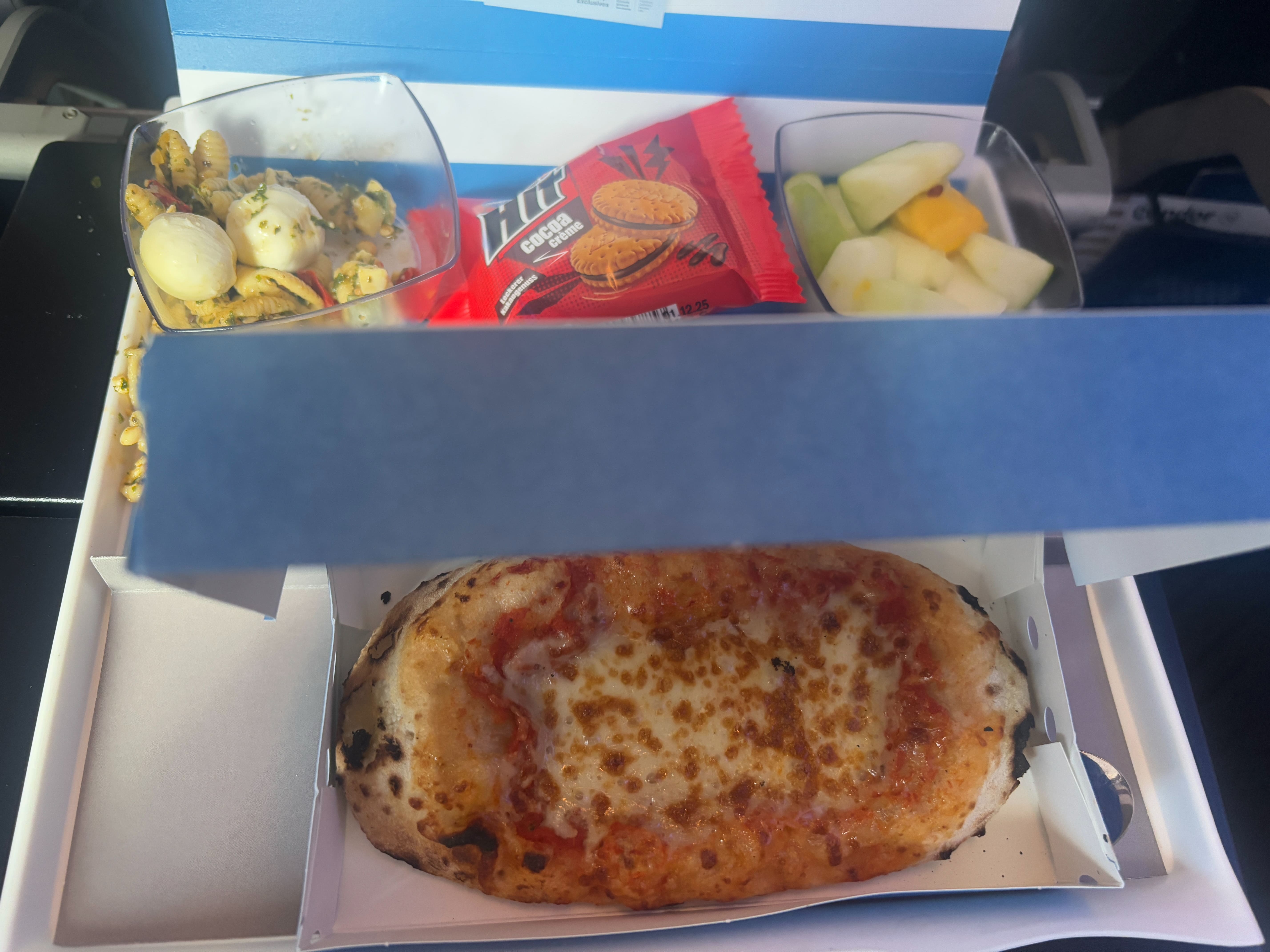 Pre-landing snack of pizza, pasta salad, sliced apples, and a packaged cookie, served on a single tray.