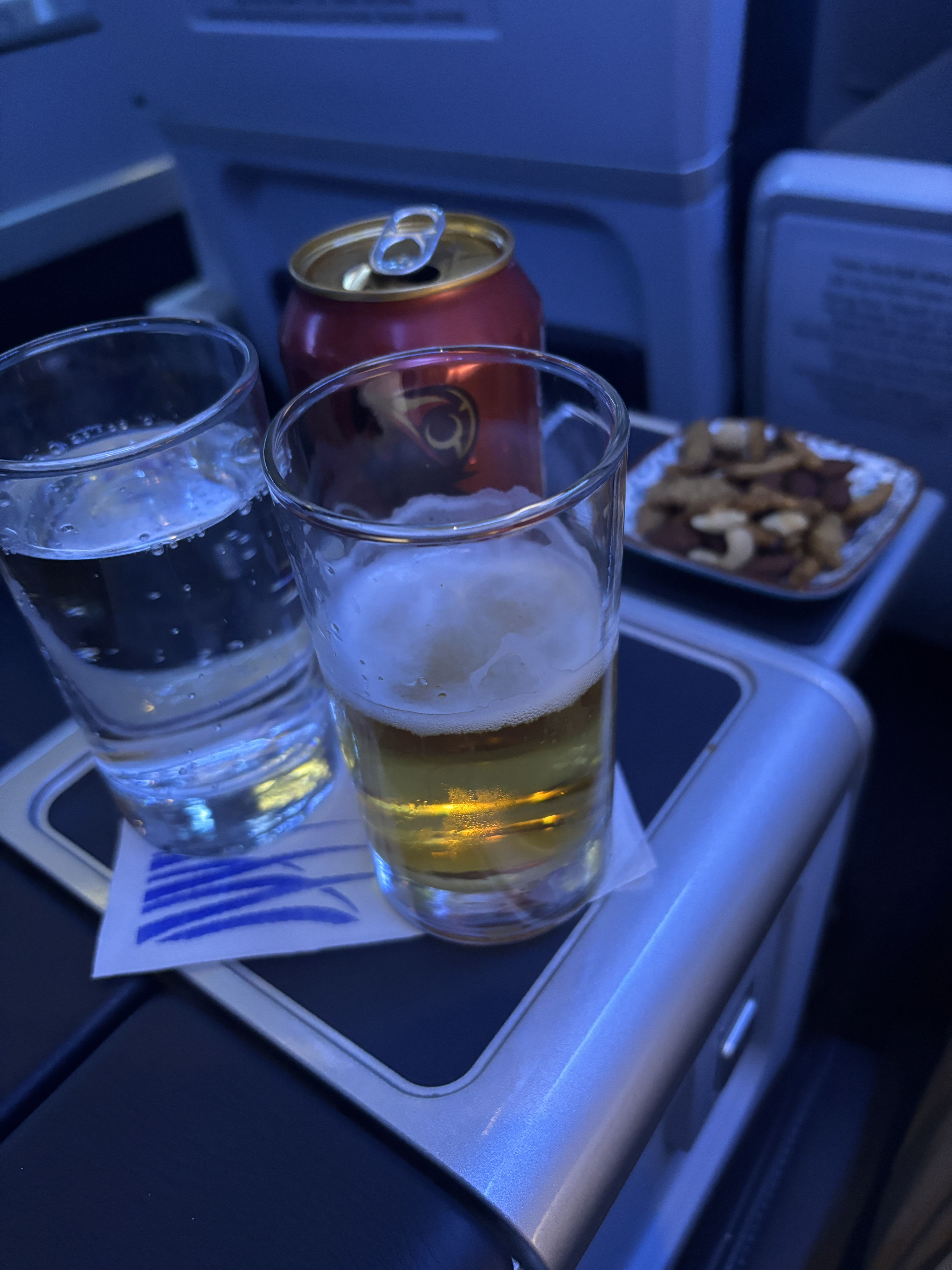 Glass of Balboa beer, water, and ramekin of nuts resting on an armrest drink holder.