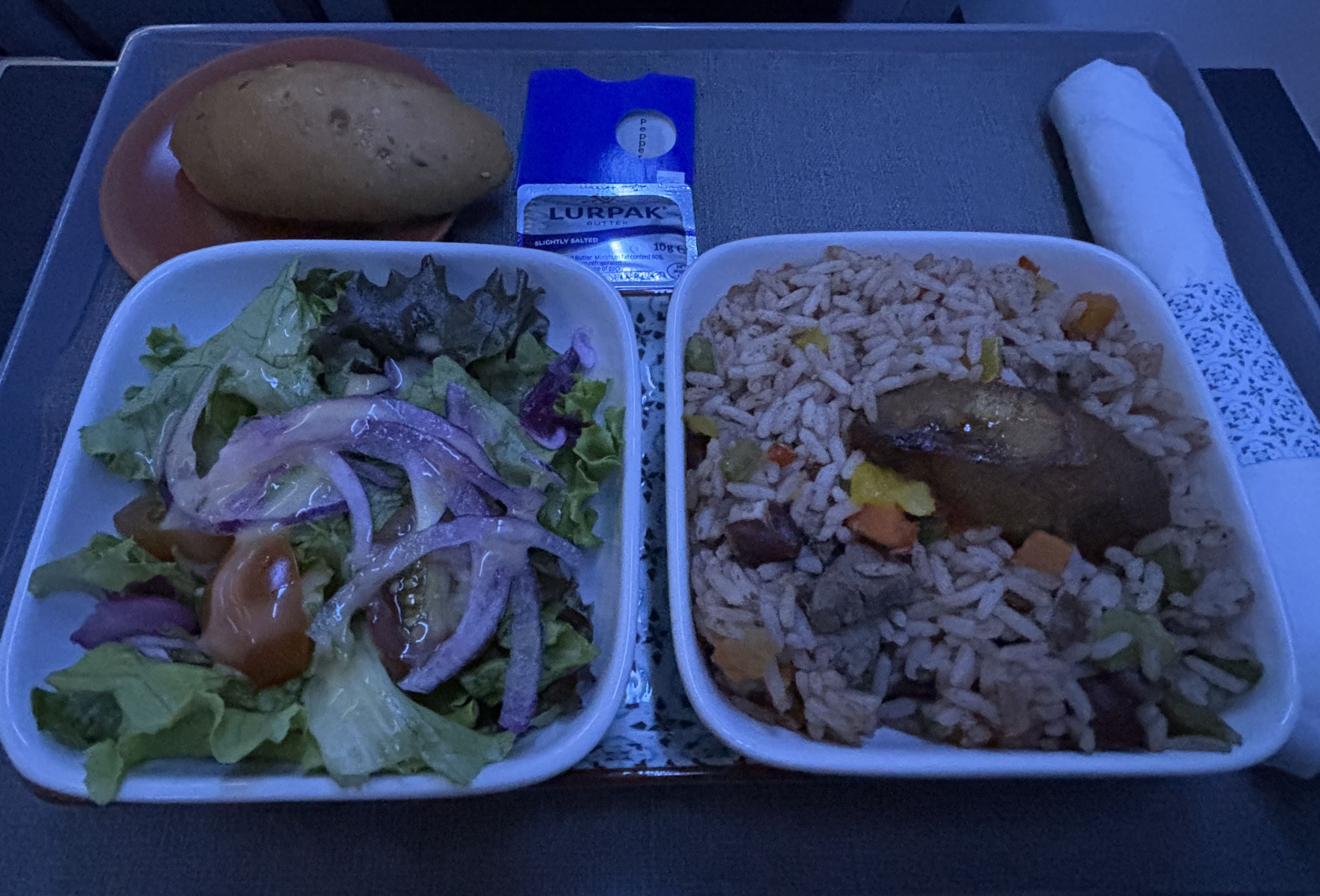 Dinner tray with bread roll, garden salad, and rice with beef and fried plantain.