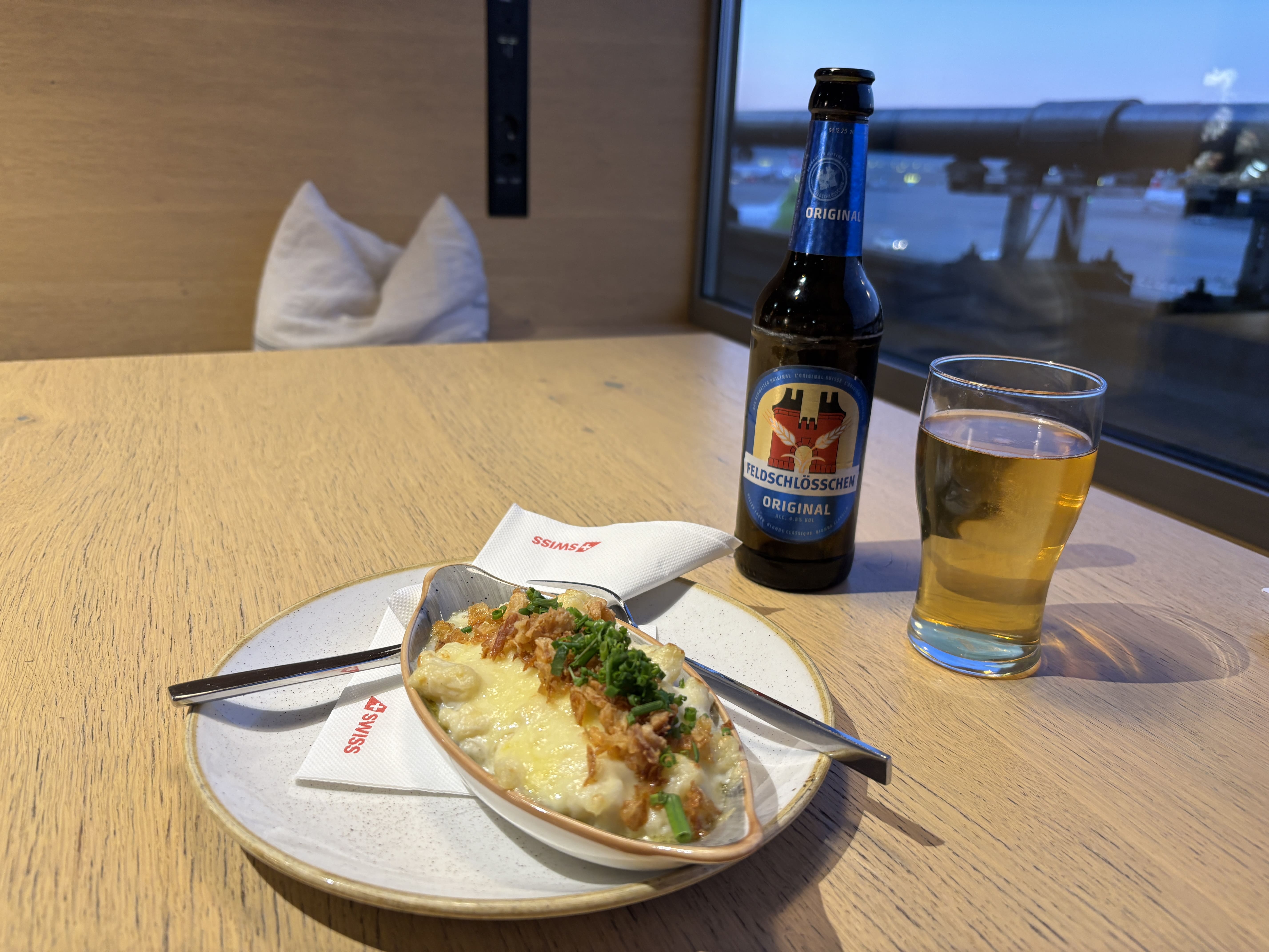 Cheese spätzle on a wodden table next to a poured bottle of beer.