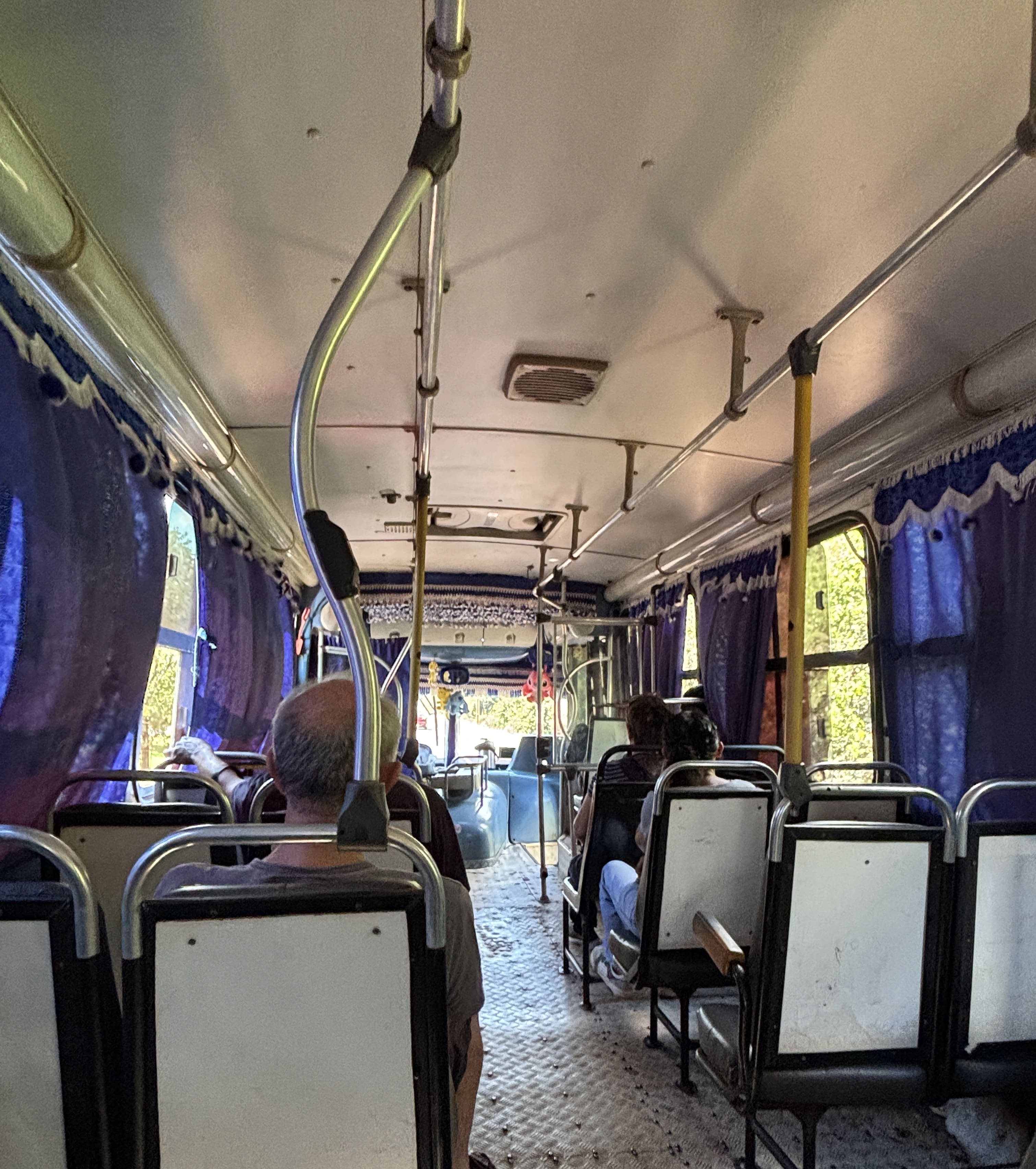 Interior of a colectivo, showing 2-2 seating with open windows mostly covered by blue curtains.
