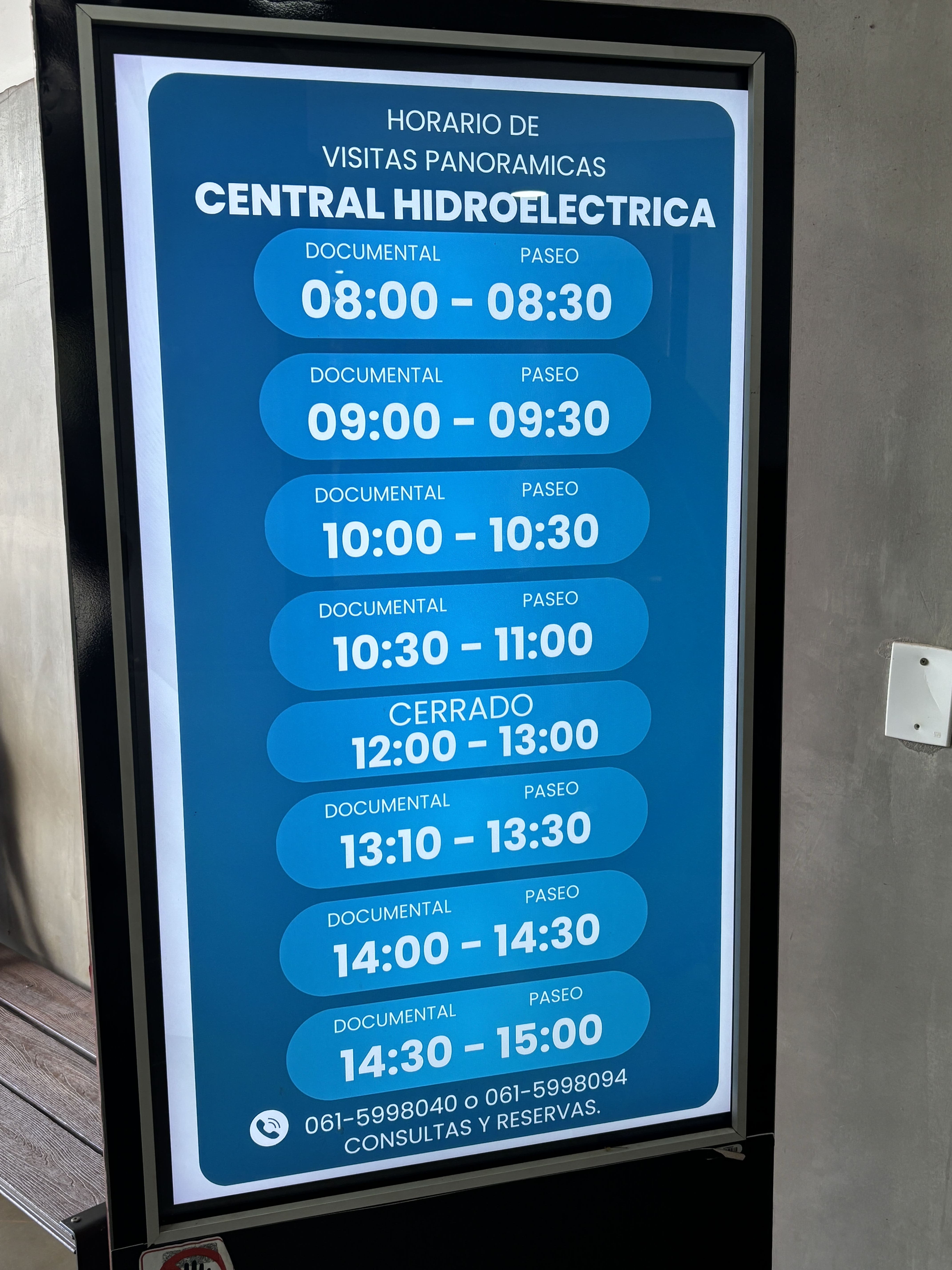 Display sign showing tour times at Itaipú Dam: 08:30, 09:30, 10:30, 11:00, 13:30, 14:30, 15:00.