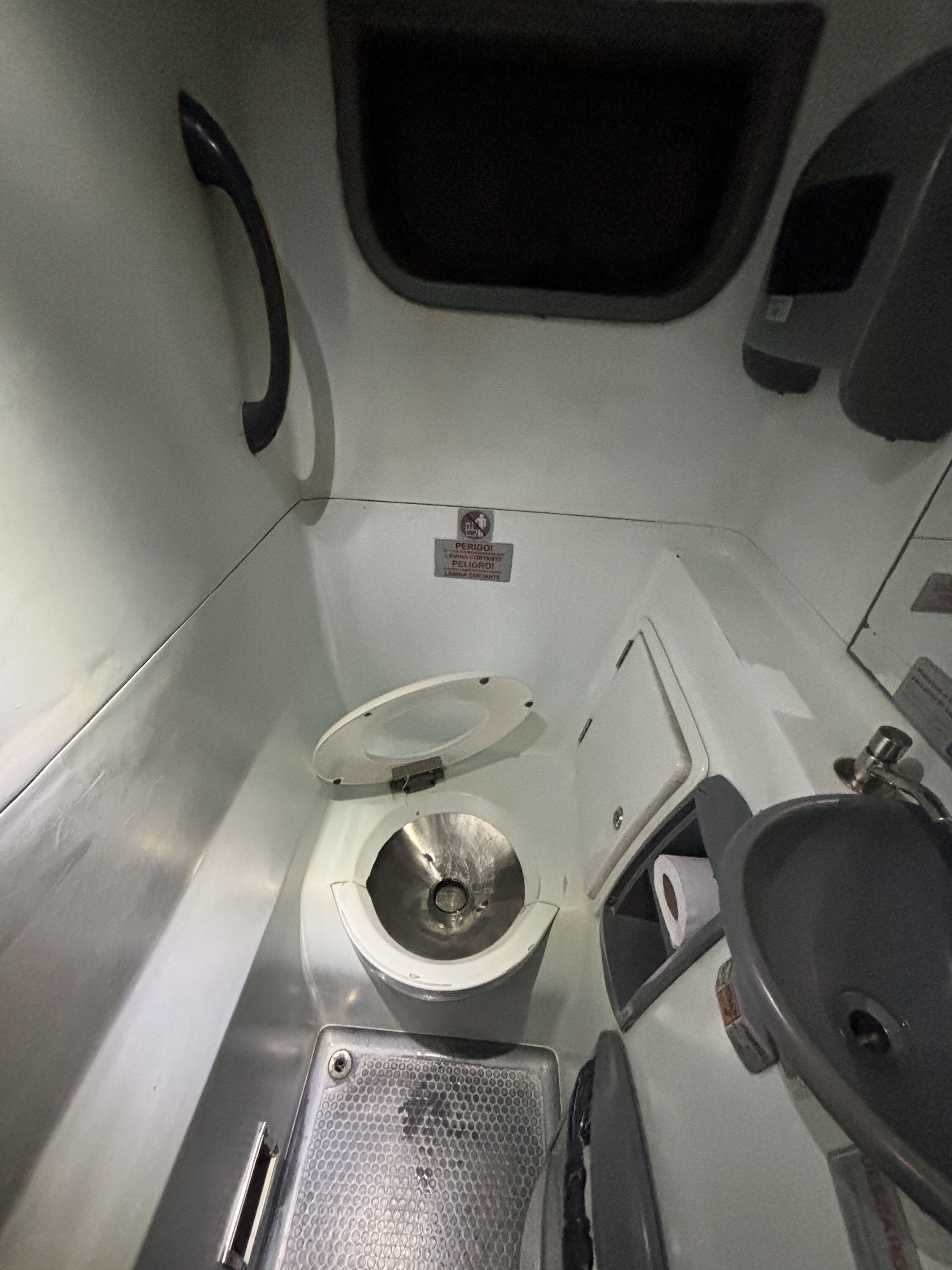 Lavatory on board a Jamjoy bus, showing a grab bar, toilet, empty towel dispenser, sink without soap, and toilet paper roll.