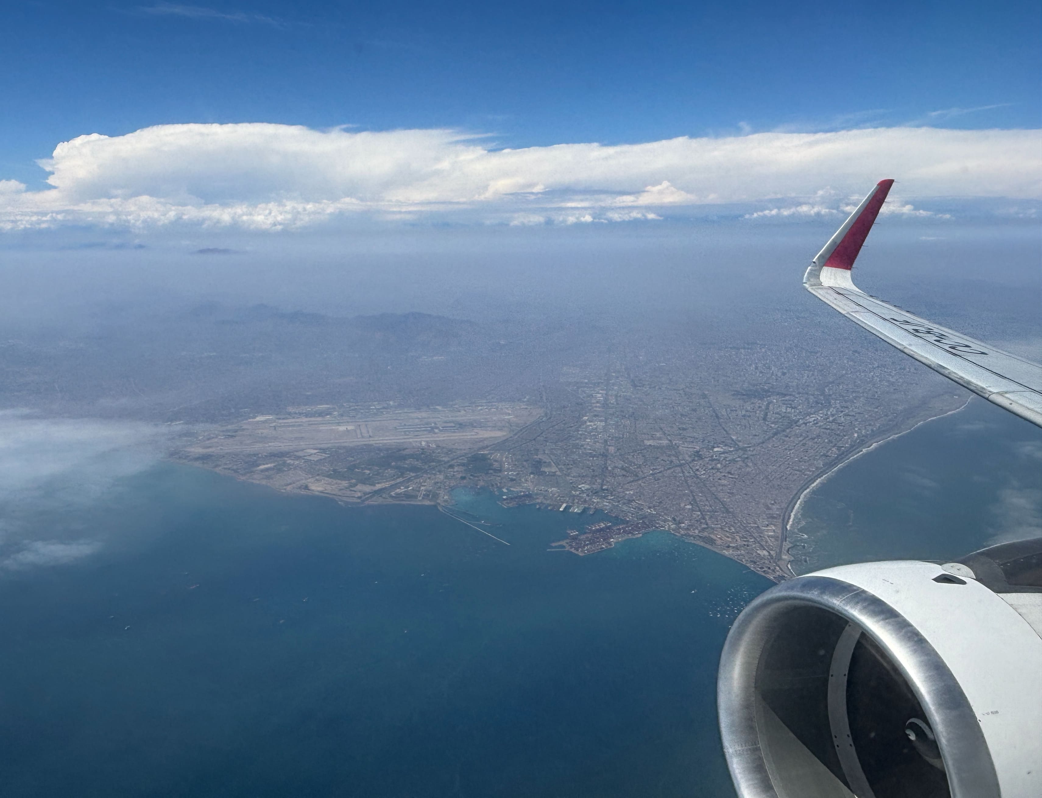 View from airplane window, showing engine and red wing tip along with a view of Lima Airport following departure.
