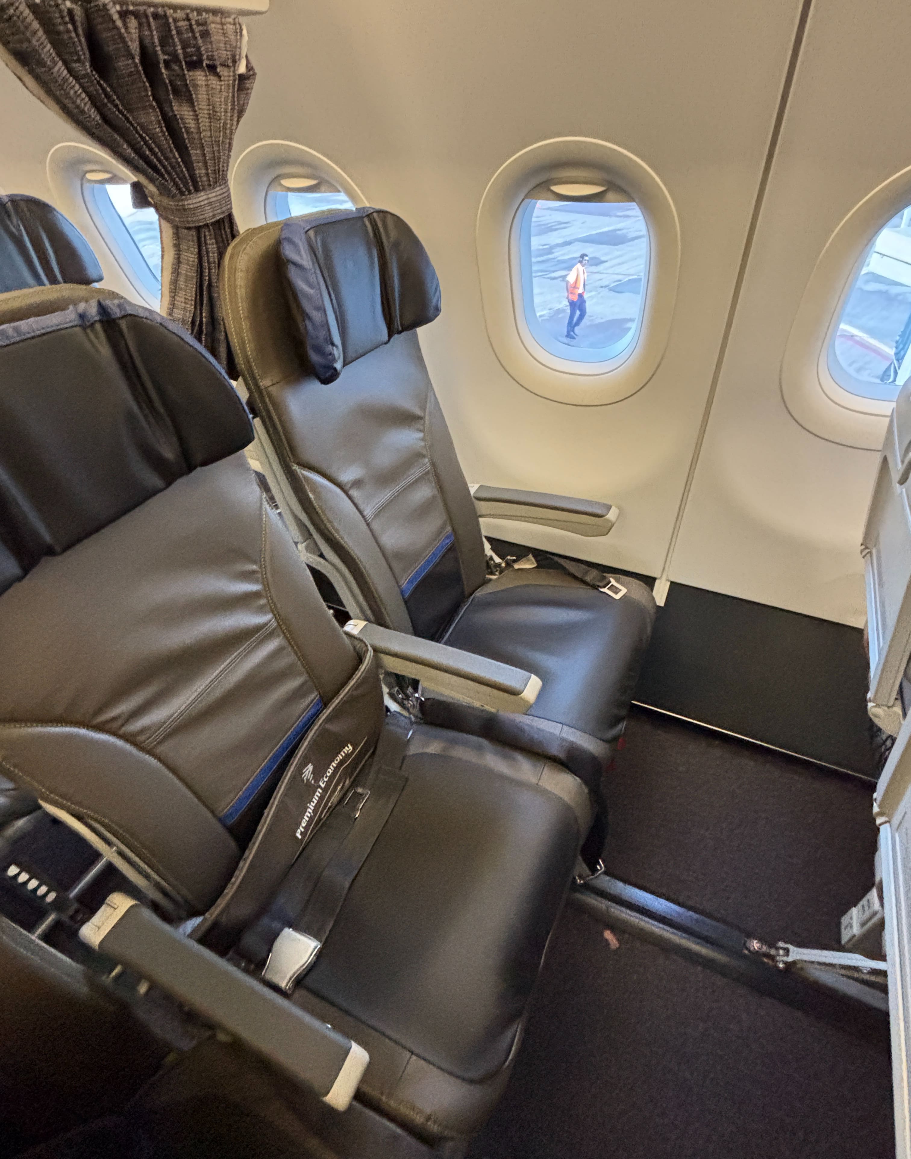 Two grey seats with blue accents, with a sign wrapped around the middle seat indicating it is blocked for premium economy.