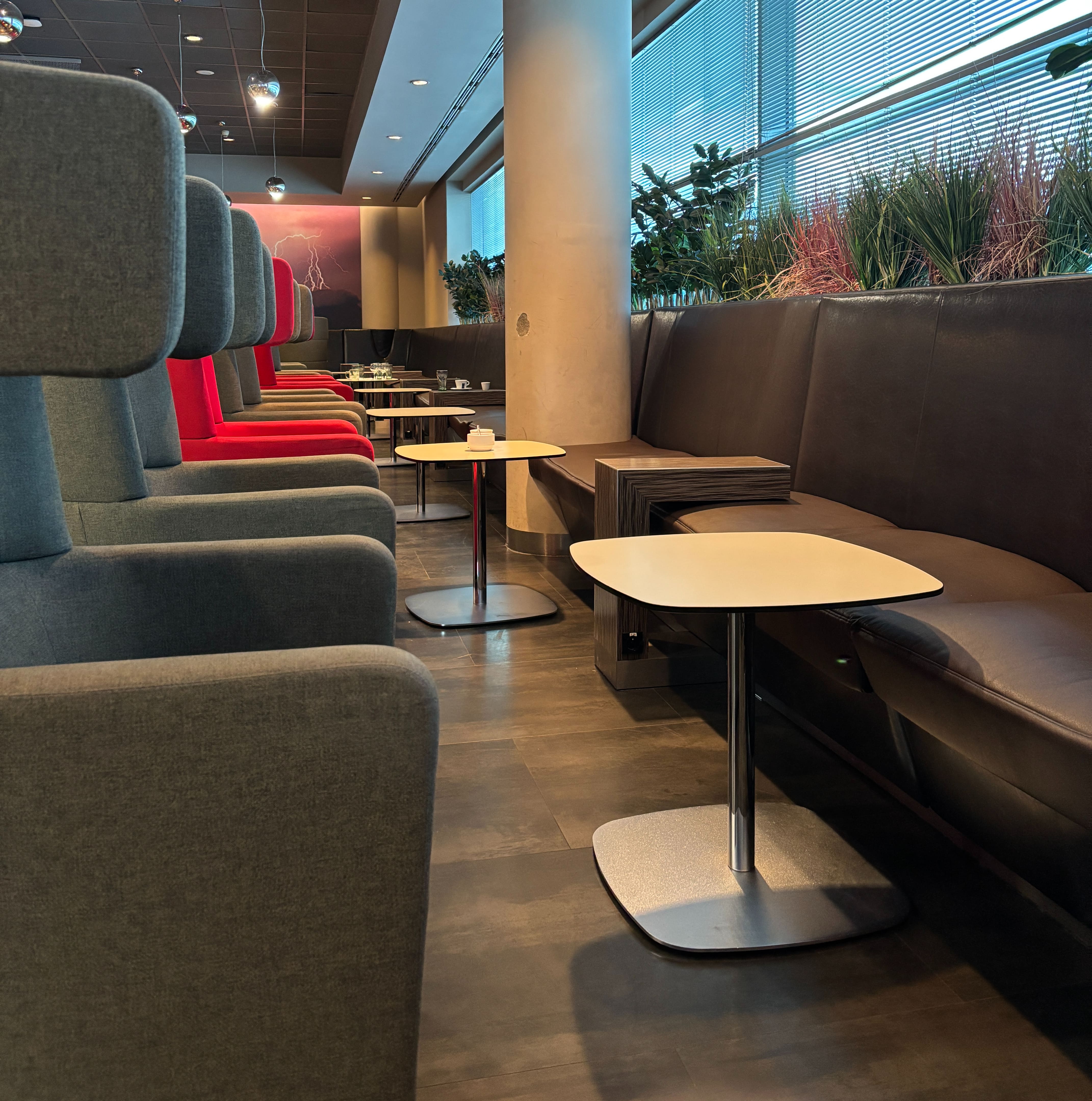 Looking down a row of empty high-back chairs facing bench-style seating, some chairs having small white tables between them and the bench.