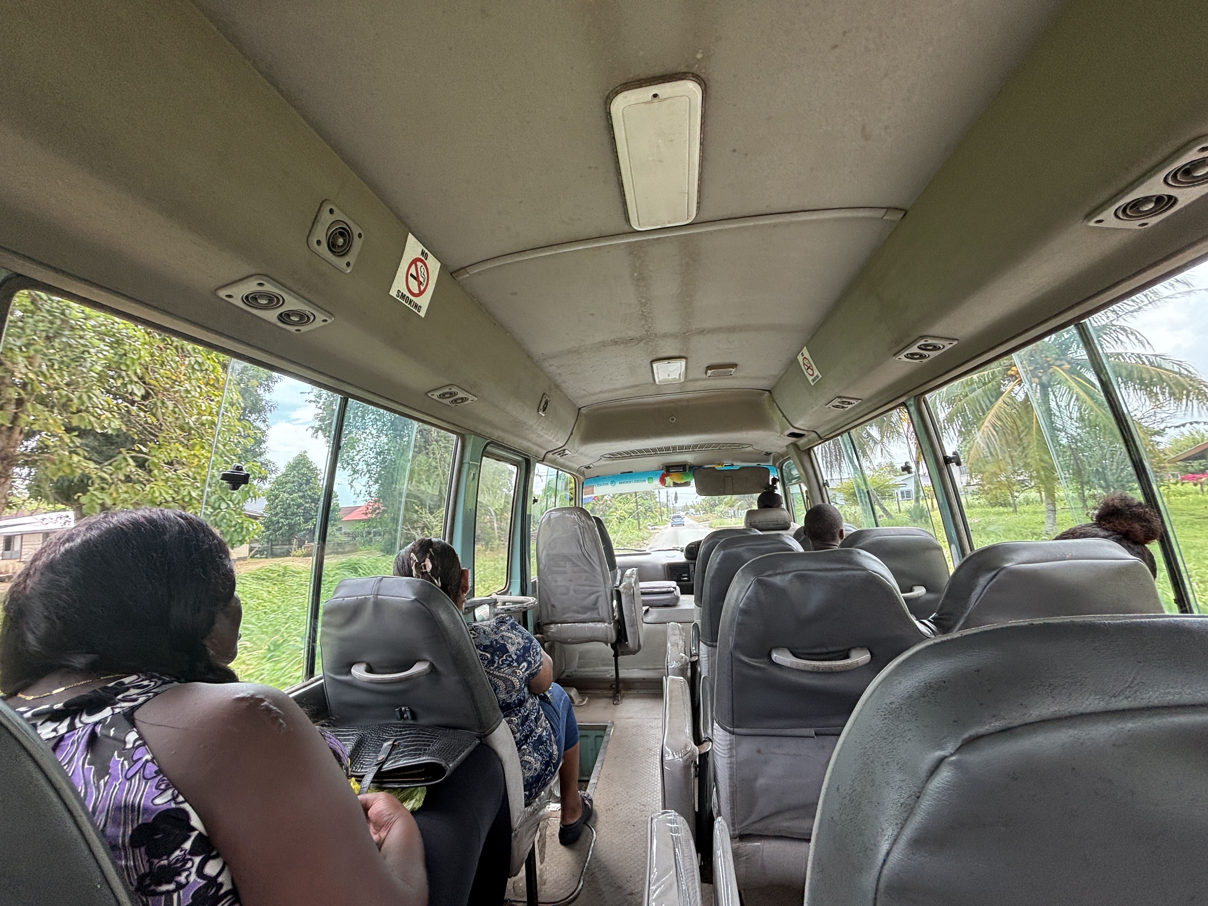 On board the bus, showing well-worn grey seats arranged 1-2 with a small aisle.