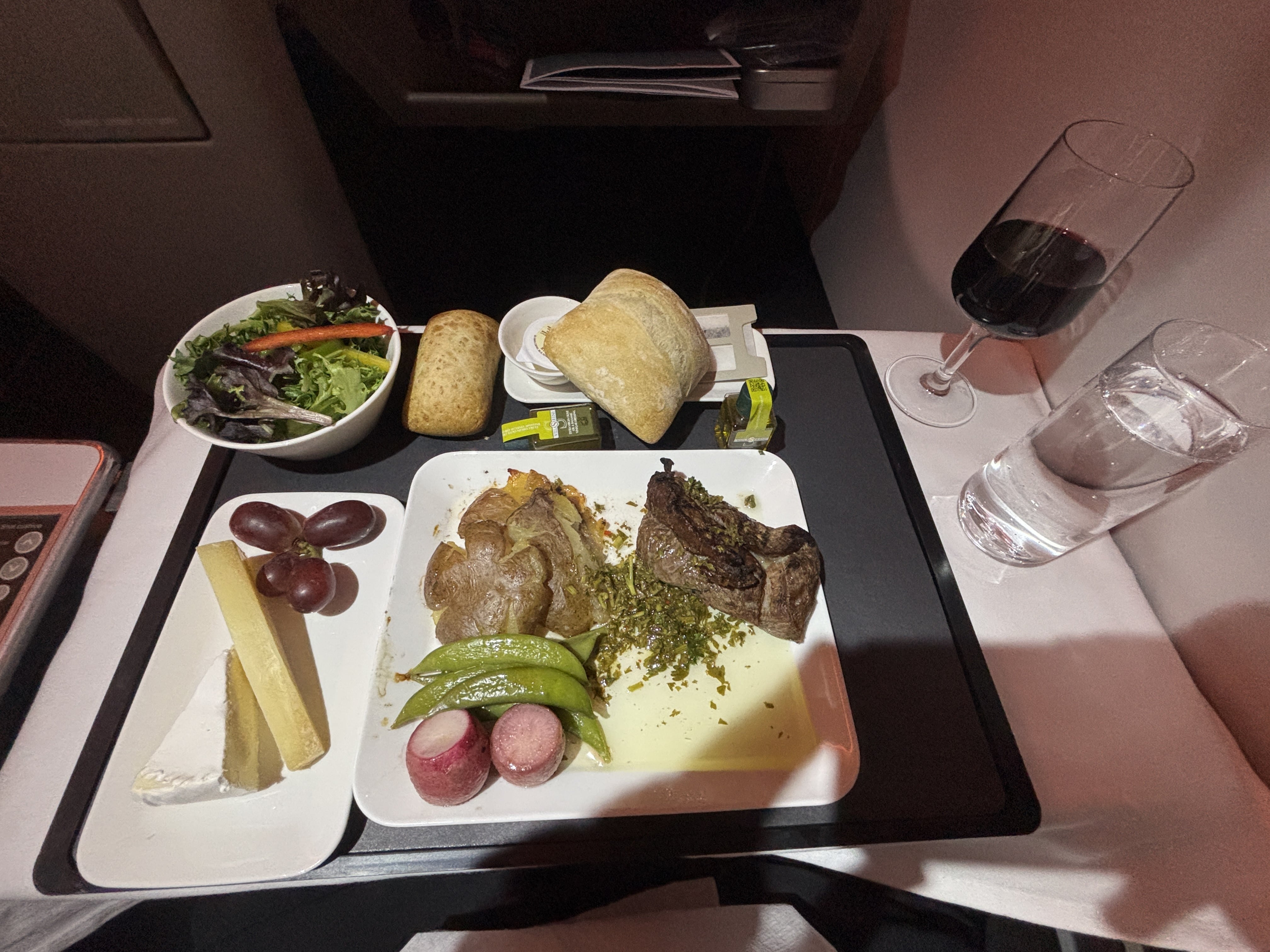 From left to right: salad bowl, cheese plate, two bread rolls, small beef filet, red wine, glass of sparkling water.