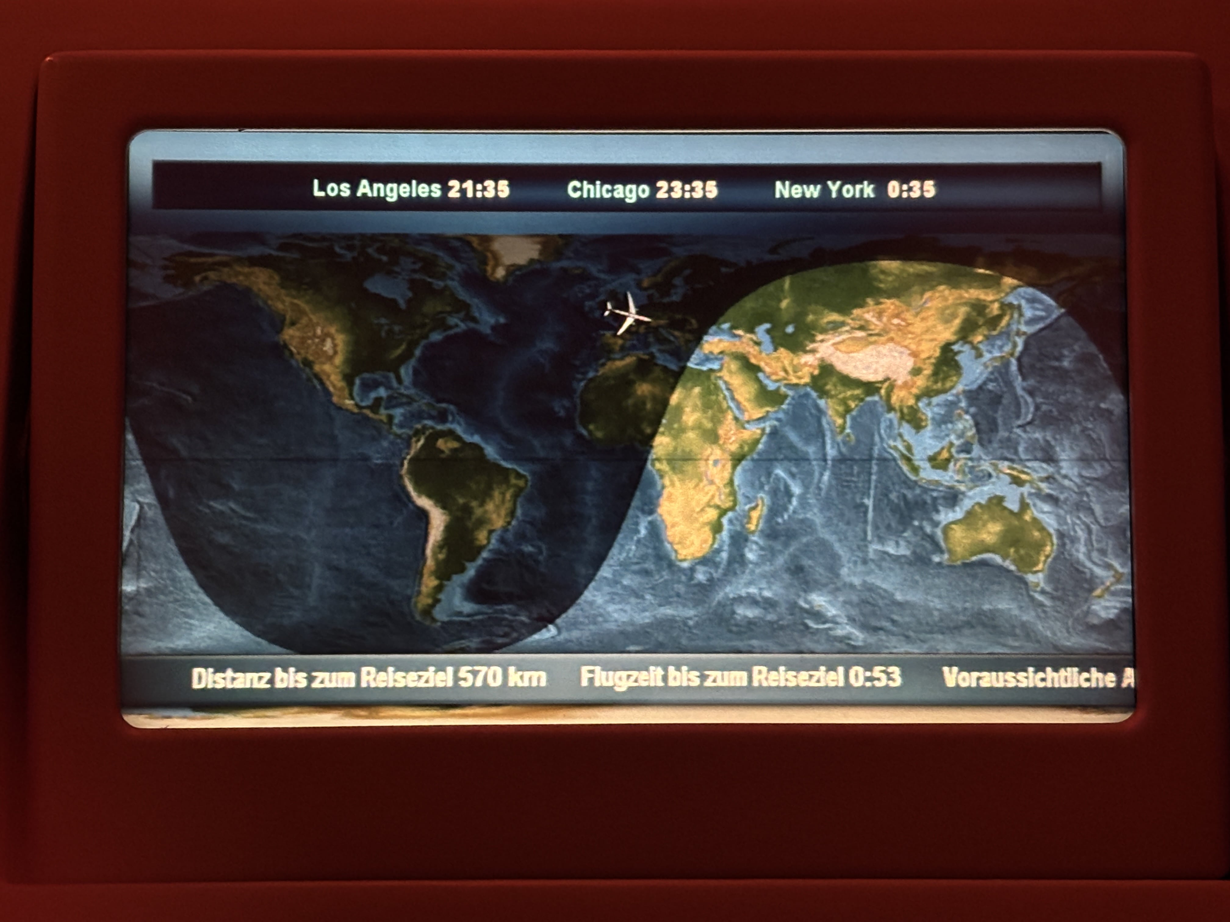 Basic, two-dimensional moving map showing plane over the United Kingdom, displaying times in Los Angeles, Chicago, and New York, as well as speed and arrival information in German.