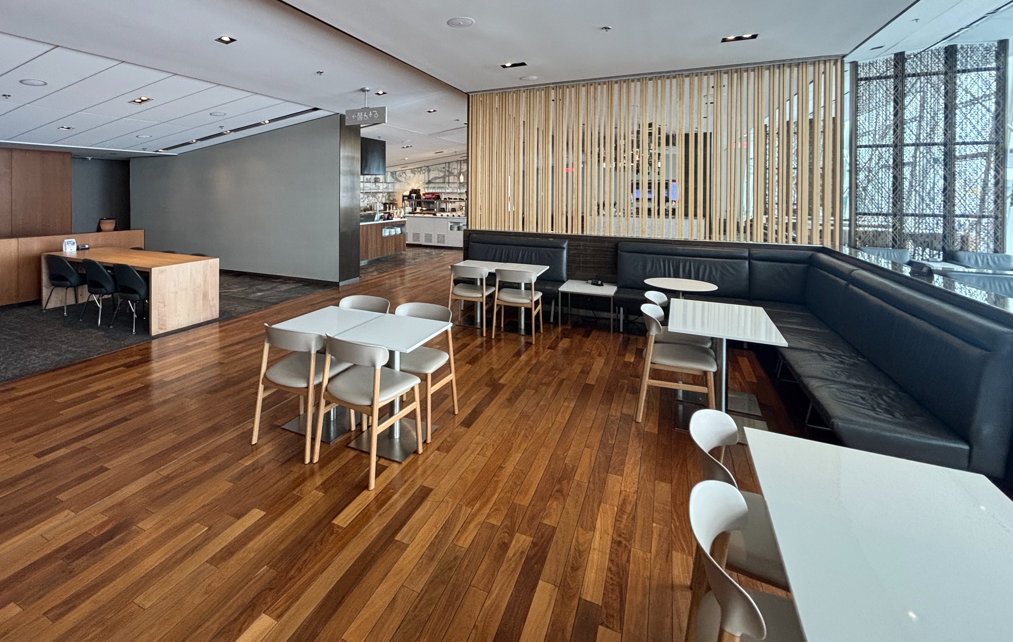 White dining chairs and tables on a brown hardwood floor, with buffet in the background.
