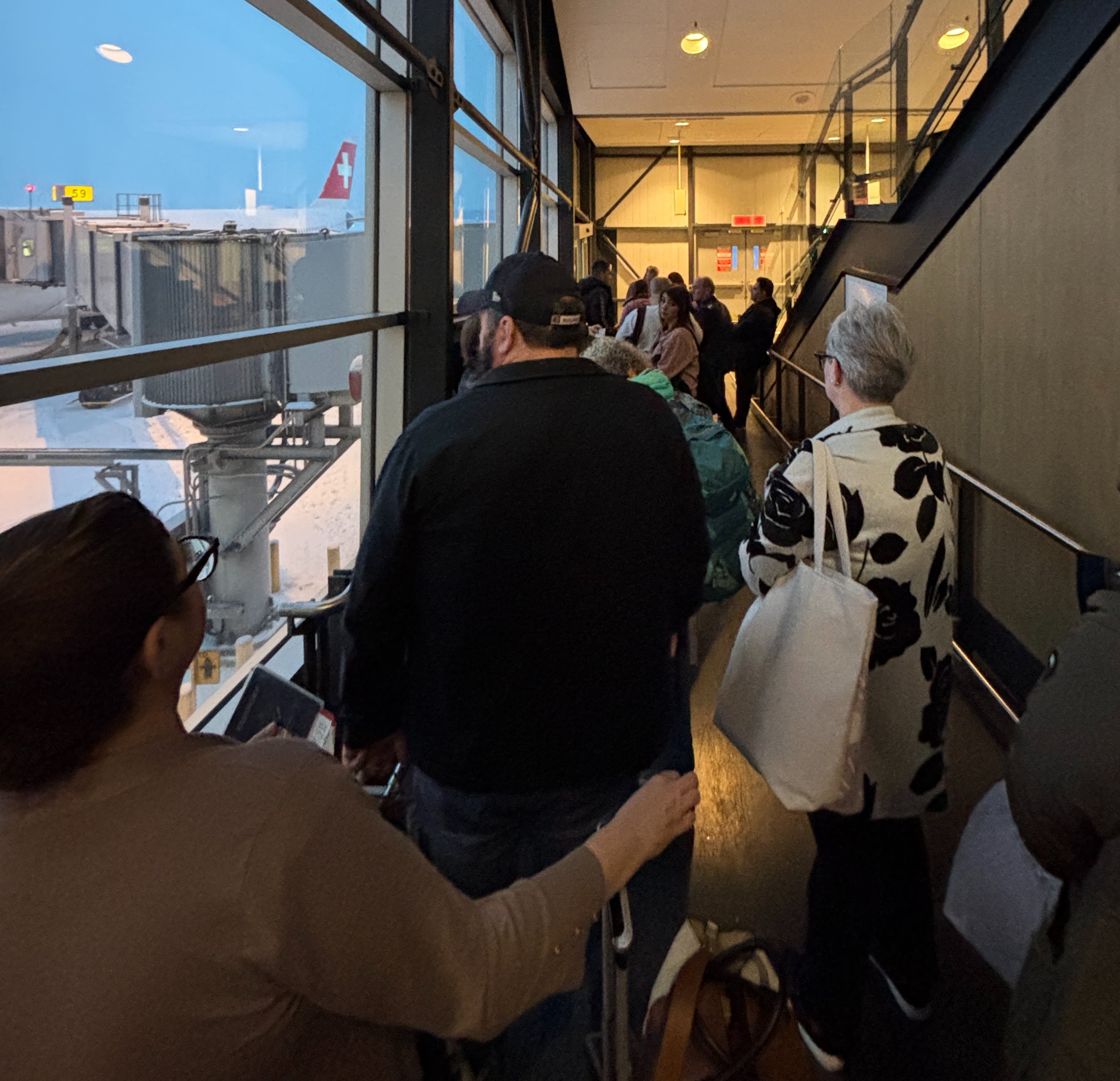 People standing in line on a jetbridge, SWISS tailfin visible in background.