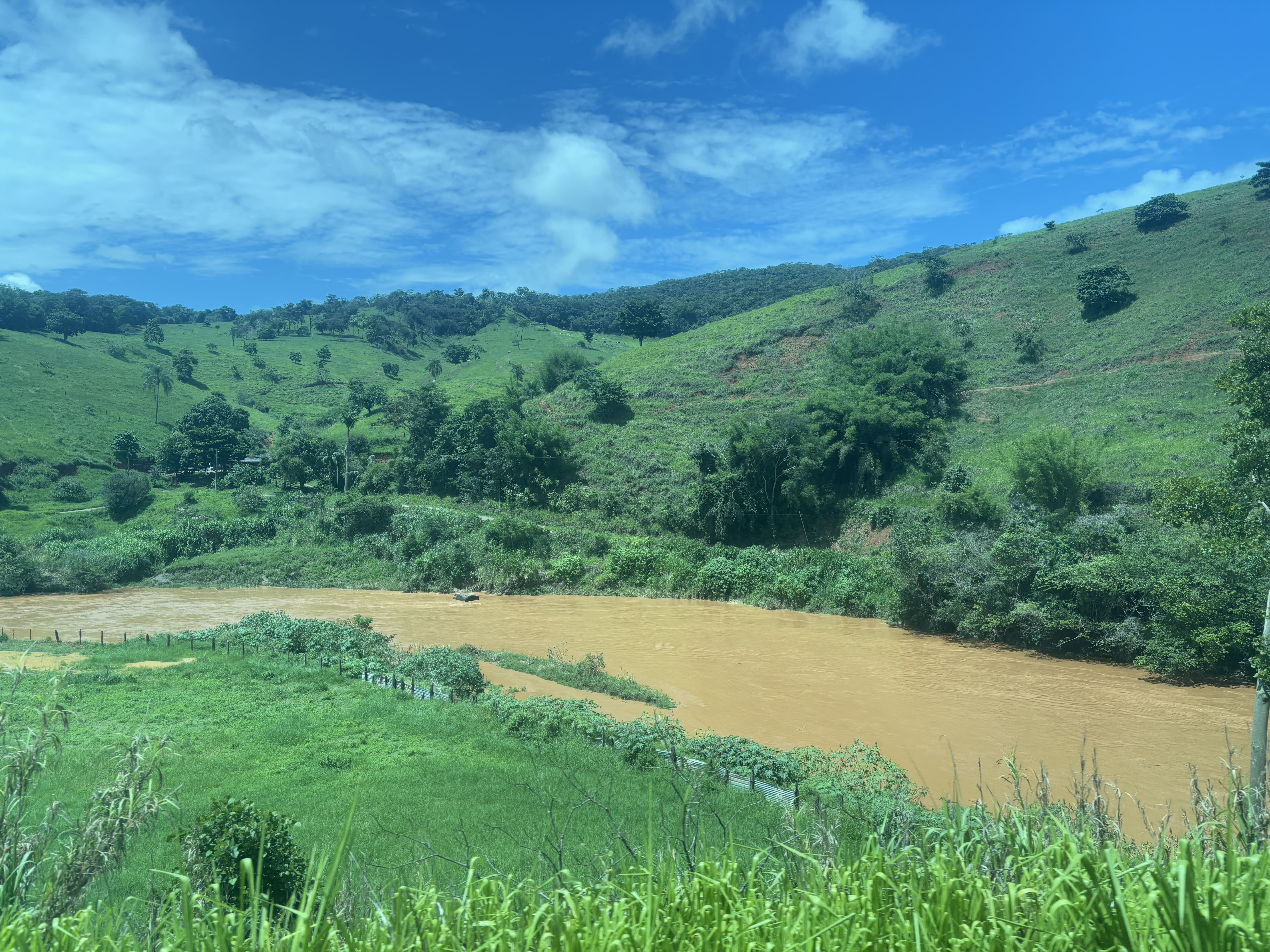 Scenery along the route, showing a brown river surrounded by green hills.