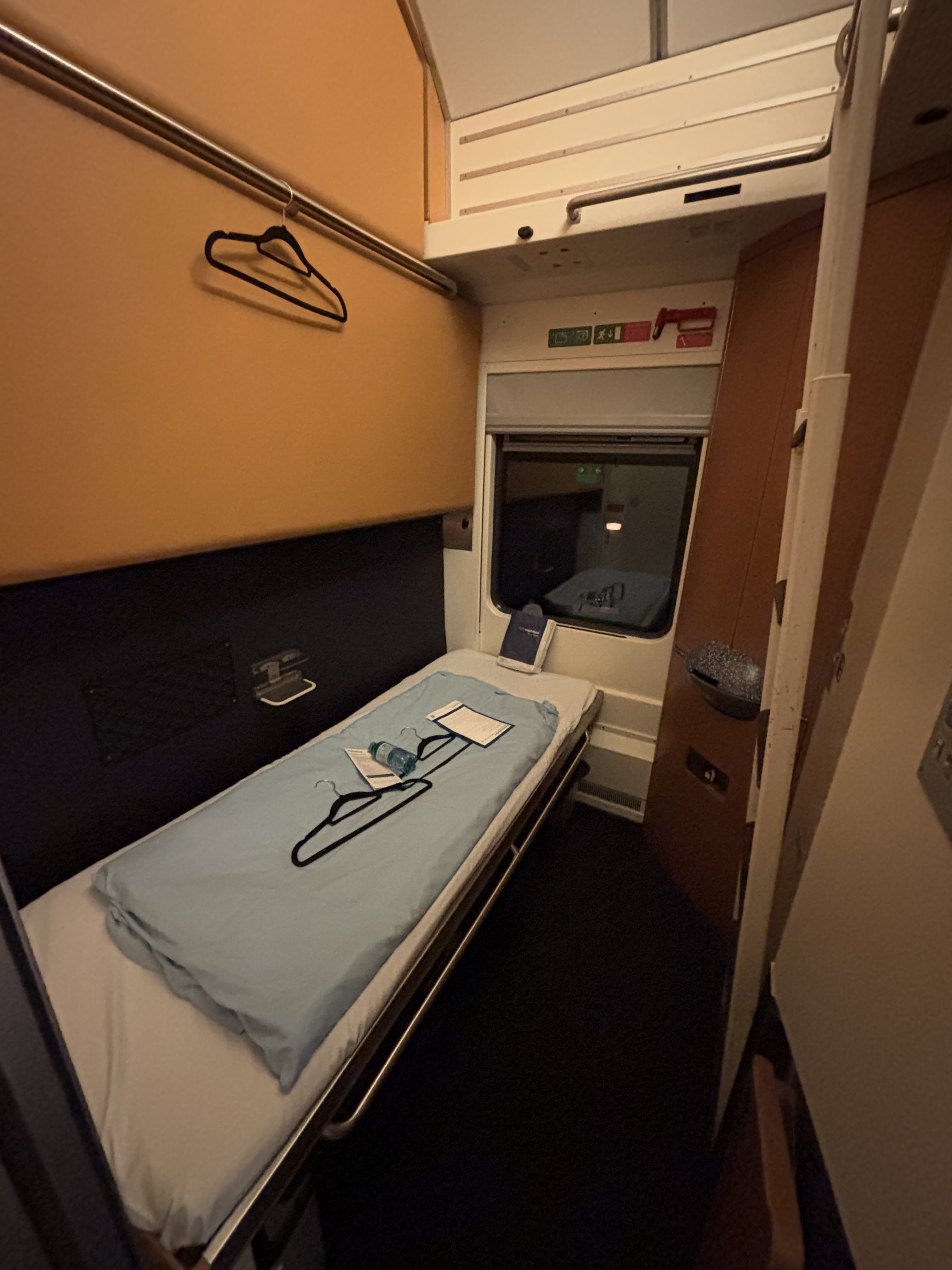 View of an empty sleeper cabin, with one bed folded down, two hangers and one water bottle resting on the folded duvet.
