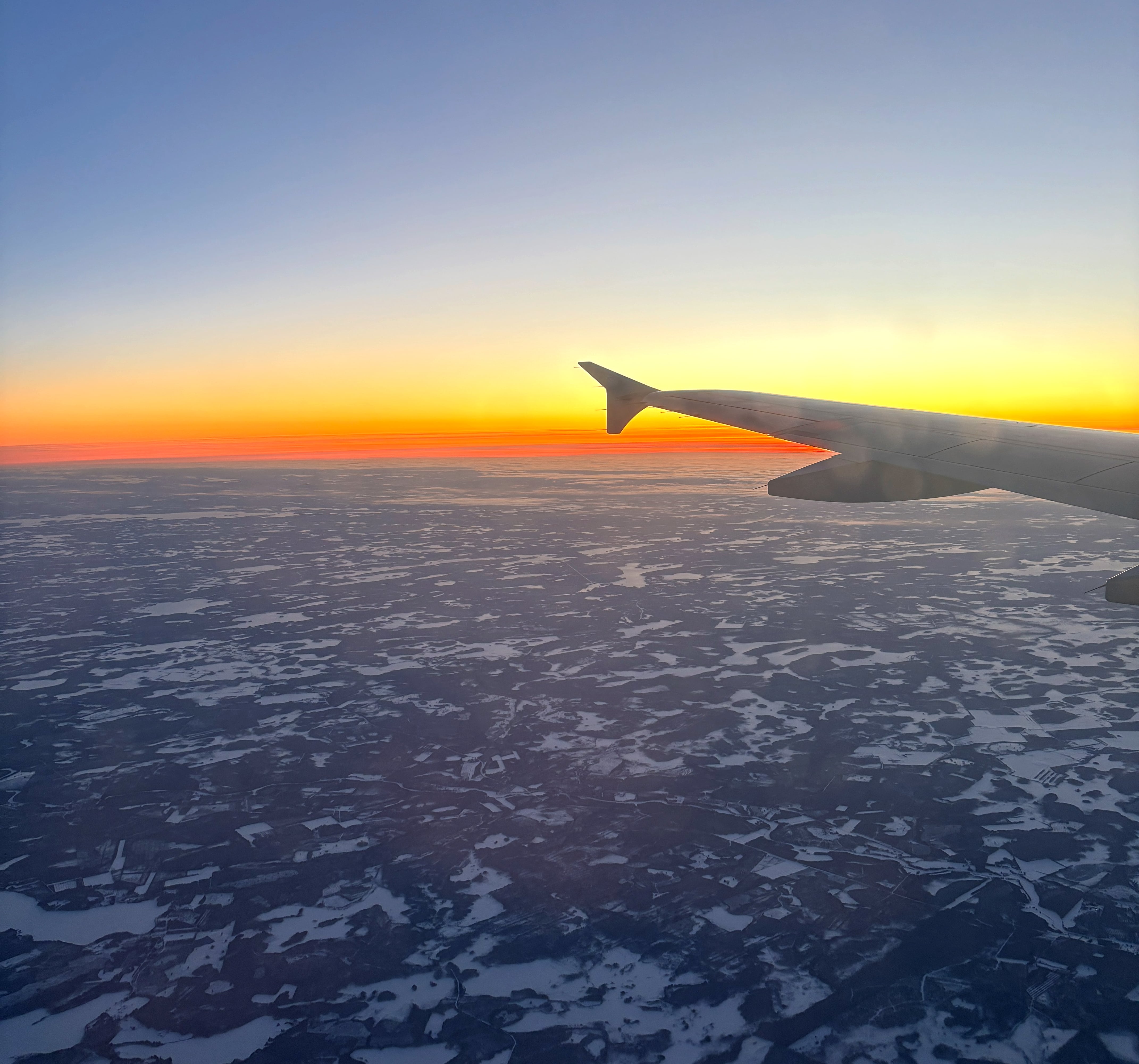 Line of vibrant orange against an inky sky as the Sun rises over a snowswept landscape, plane wing visible in centre-right.