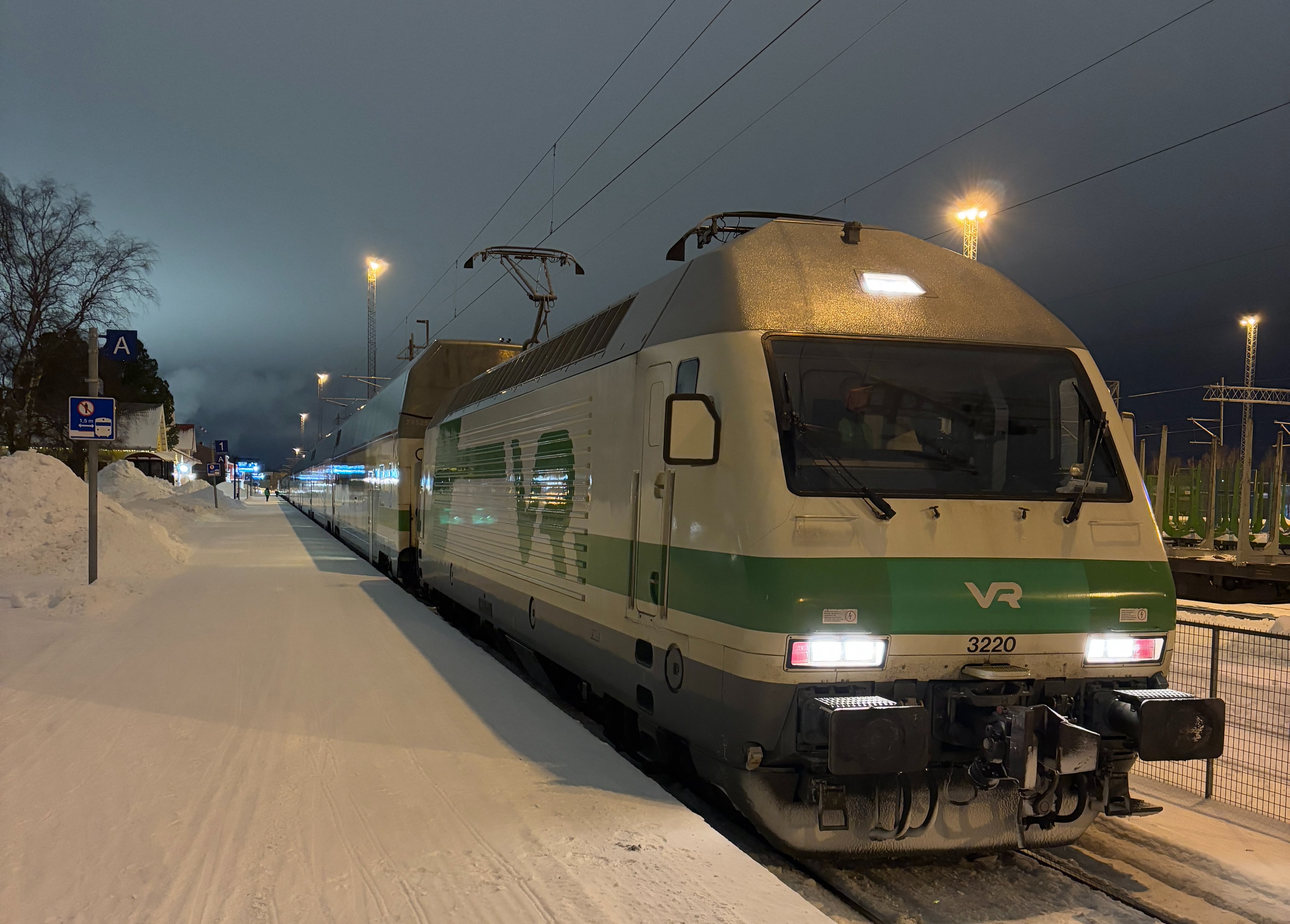 VR electric locomotive number 3220, painted white with green stripe and VR logo, standing beside a snow-covered platform.